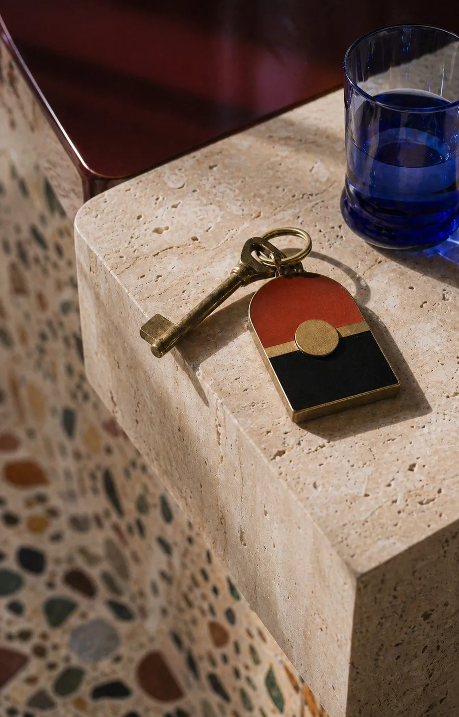 Brass key with red and black enamel fob on travertine — the threshold of a room