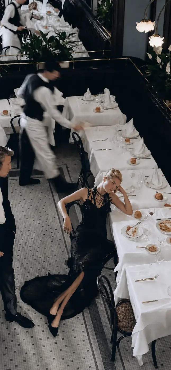 A brasserie mid-service seen from above: a seated guest still at a finished table while a waiter crosses the room in motion