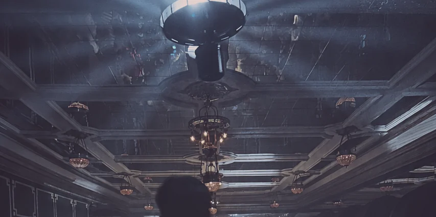 A grand historic ceiling — chandeliers, coffered plaster — cut through by the beams of a modern lighting rig