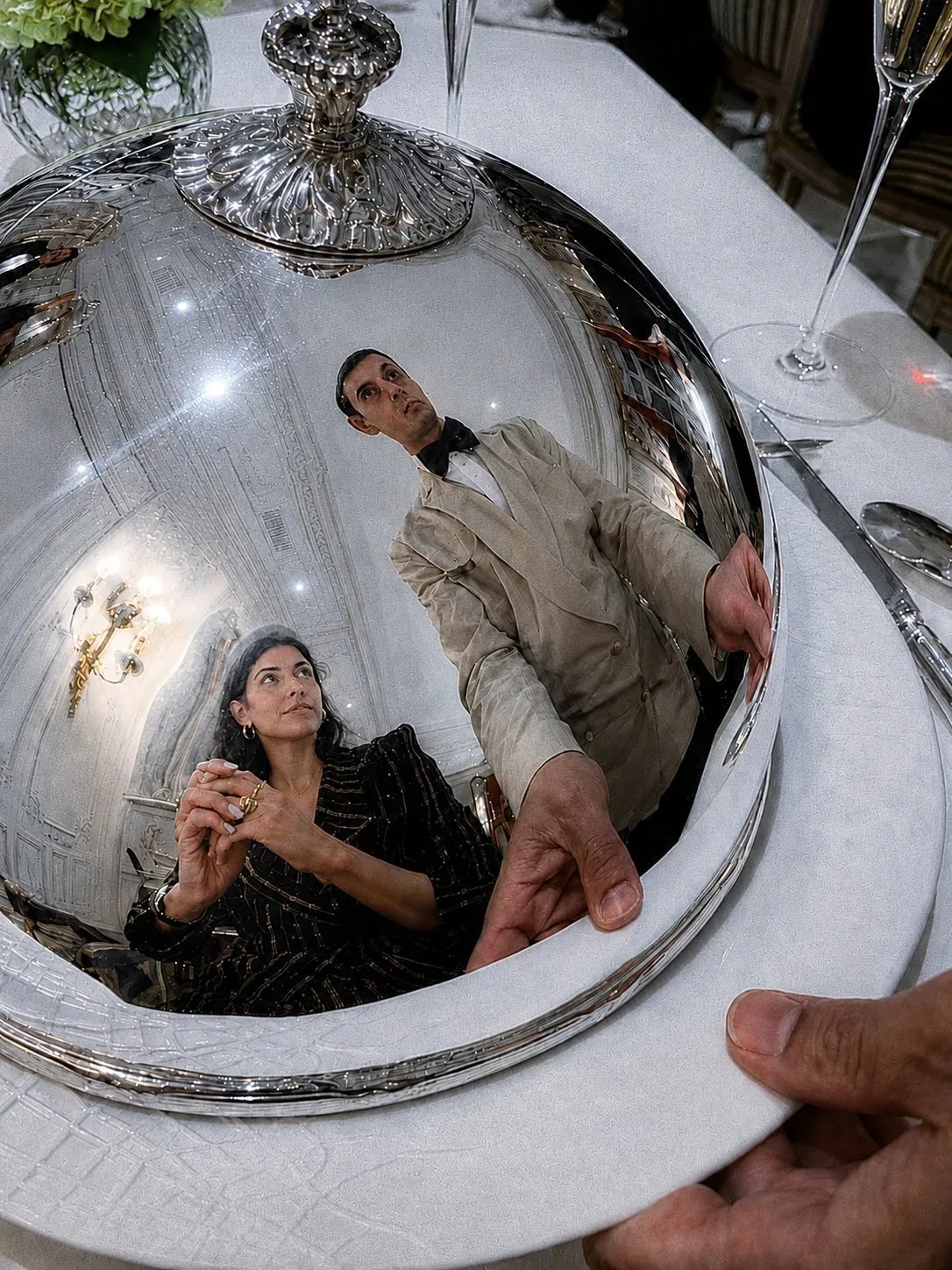 Two guests reflected in a silver cloche as it is lifted