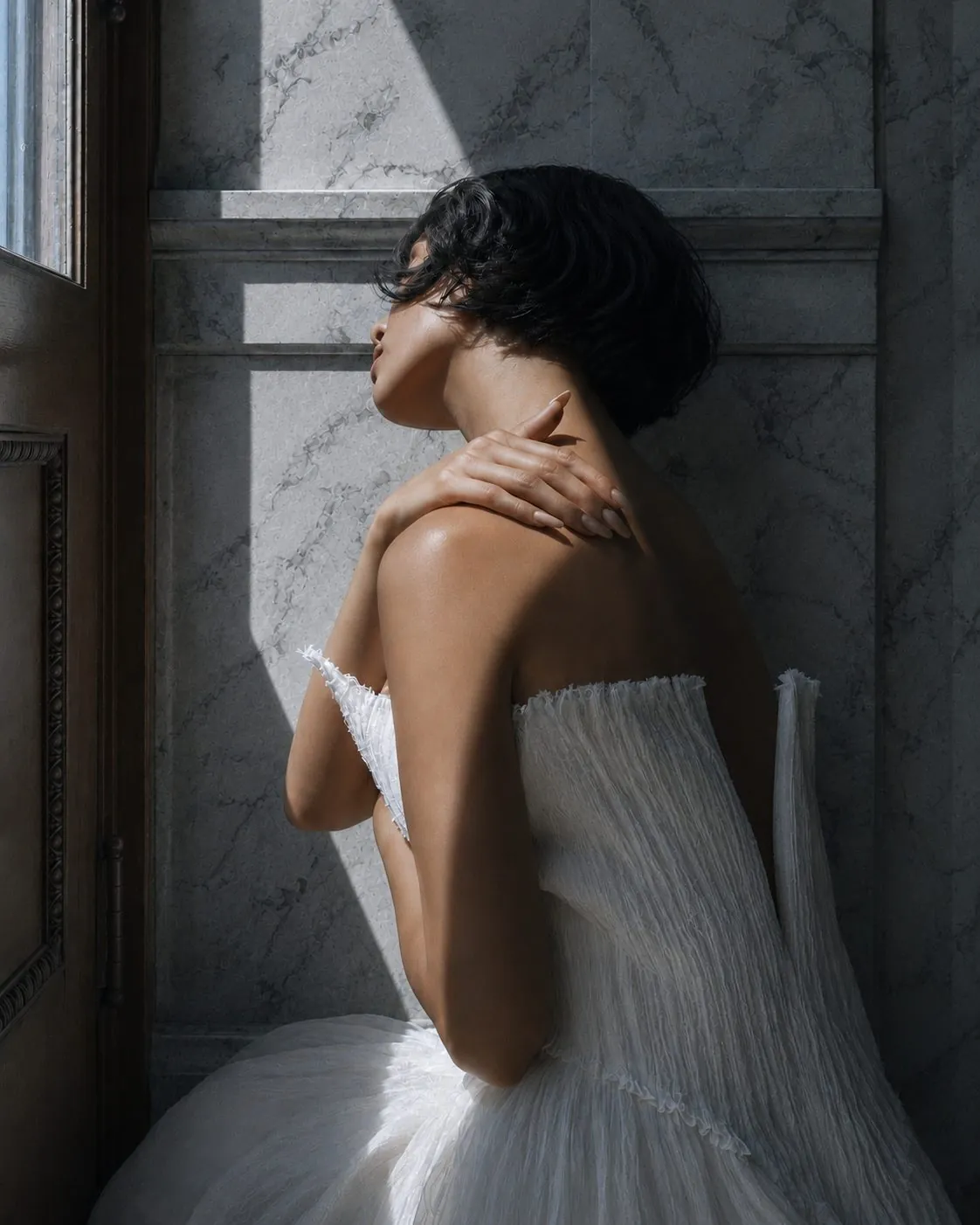 A woman holding her own shoulder against cold marble, turned away from the light
