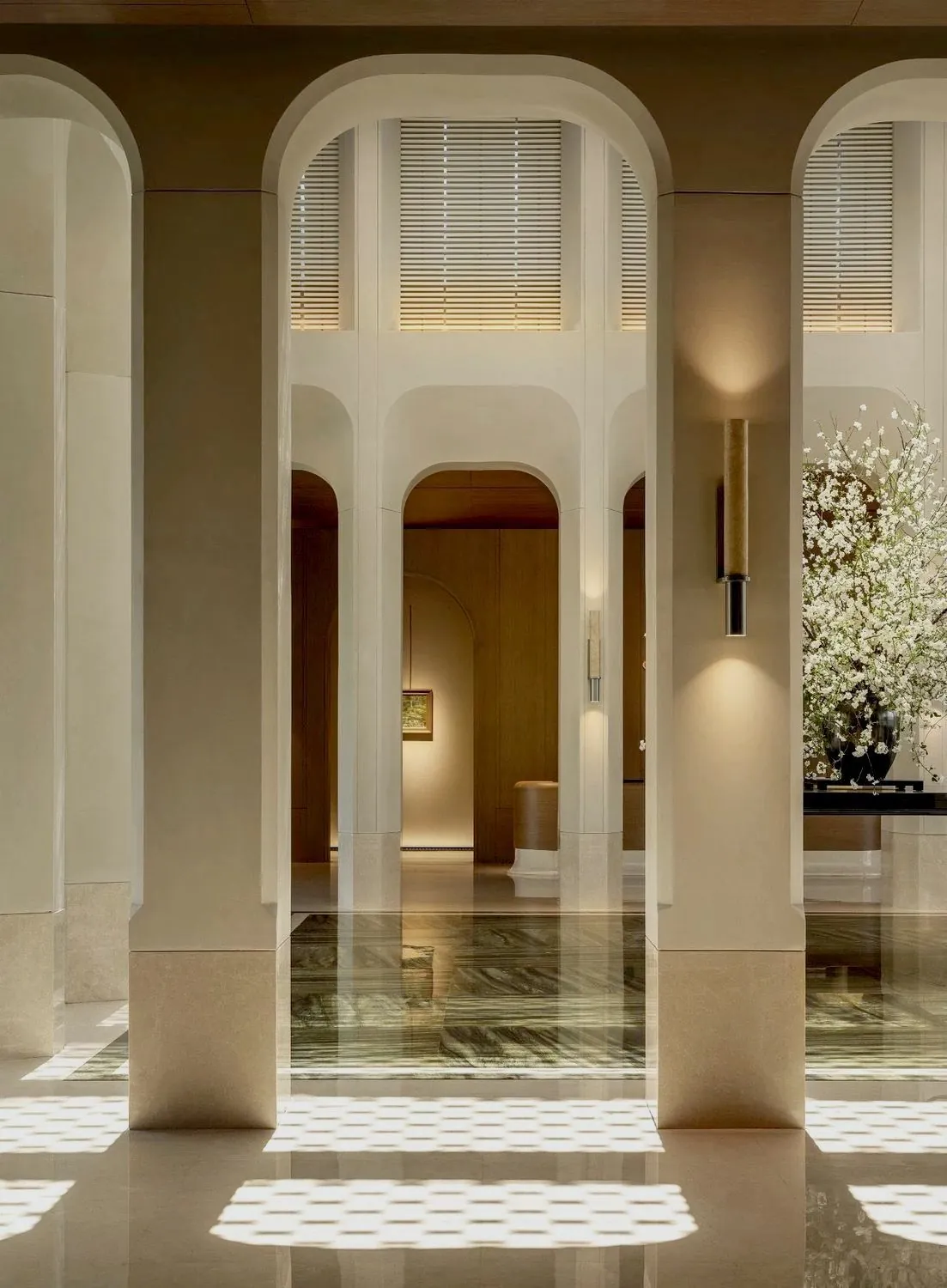The corridor of a Paris luxury hotel, light falling across marble toward the guestroom doors