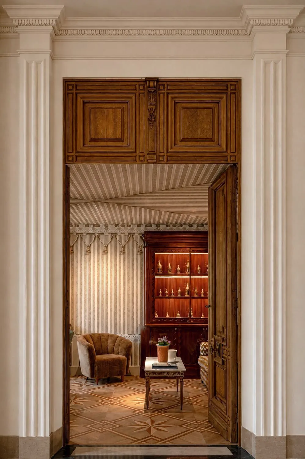 A panelled salon seen through an open door, parquet star floor, one chair and a cup