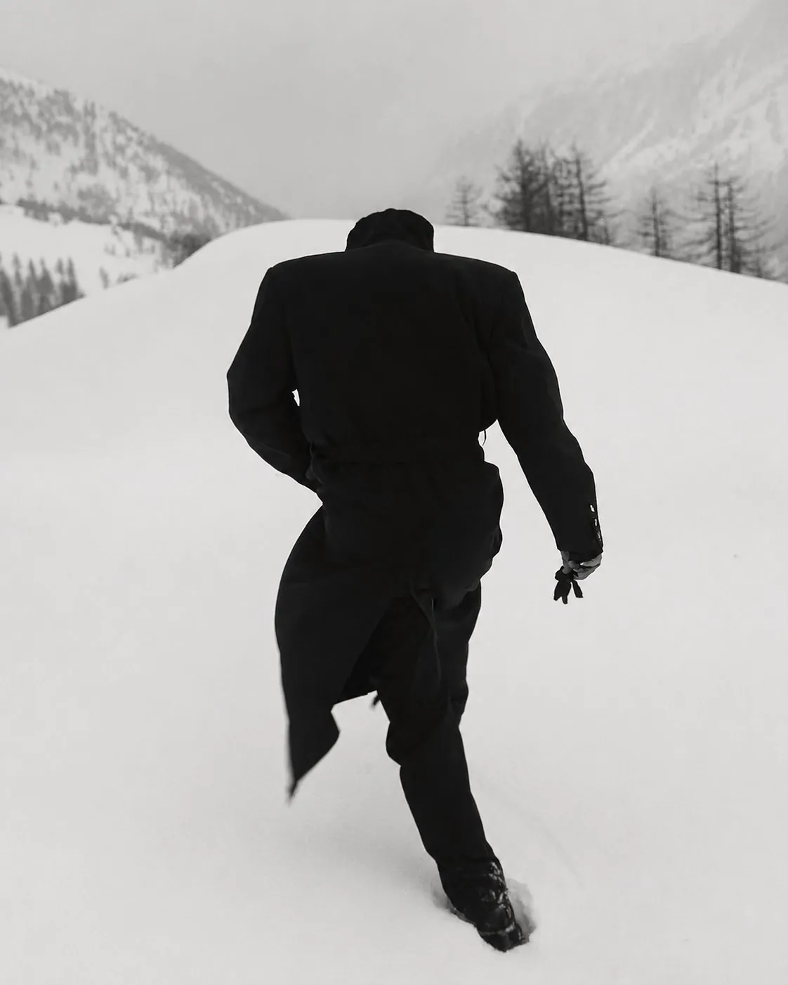 A figure in a black coat crossing deep snow, one set of tracks behind
