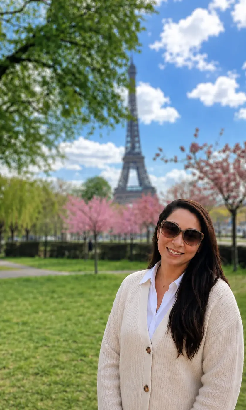 Sonia in a Paris park in spring, the Eiffel Tower and cherry blossom behind her