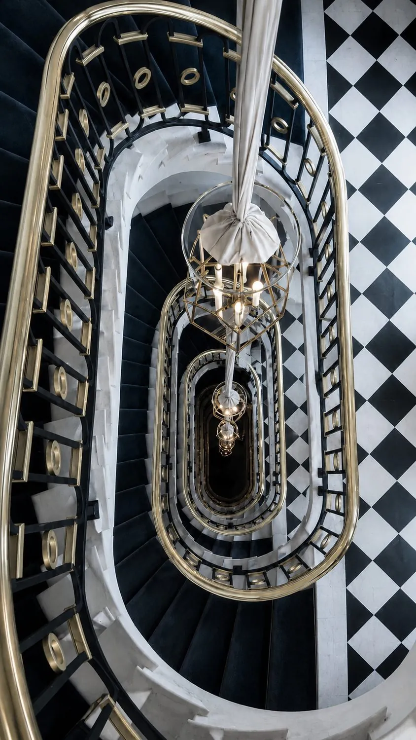 A hotel stairwell seen from above — brass, marble and repeating turns