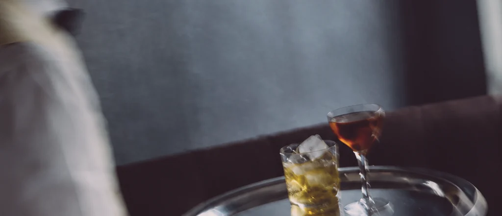 A tray of drinks carried through a dark room, the server blurred, the tray sharp